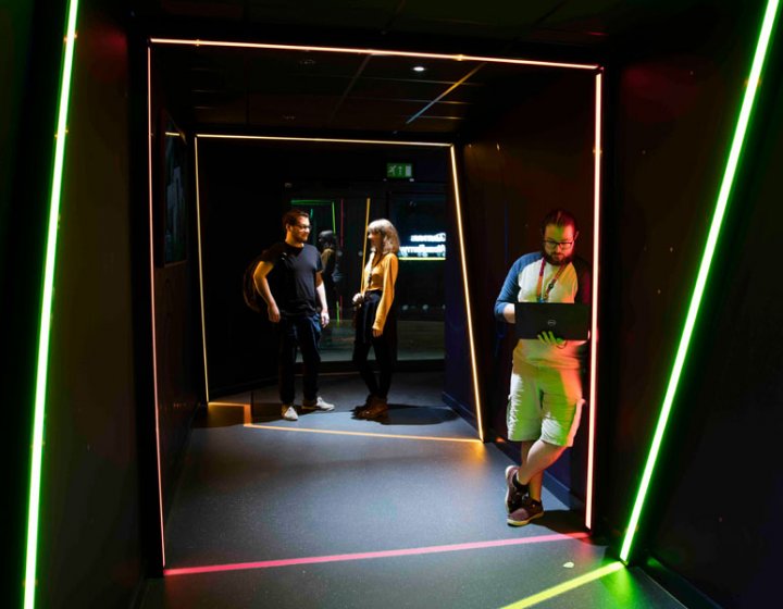 Three people standing in a dark space framed by lines of light